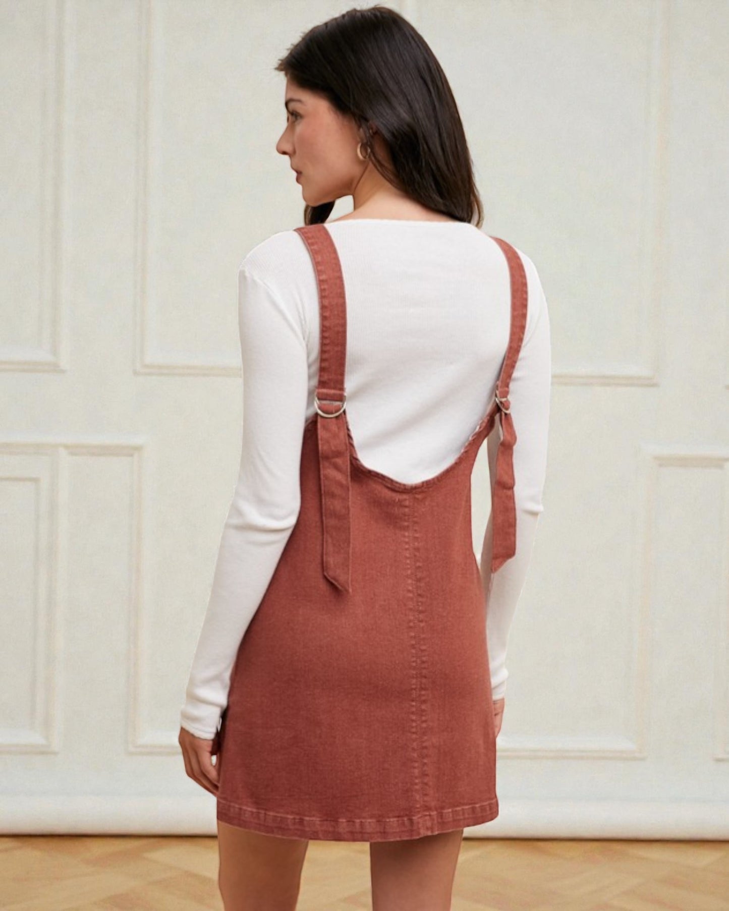 Woman wearing a white long-sleeve shirt and a brown pinafore dress against a neutral background