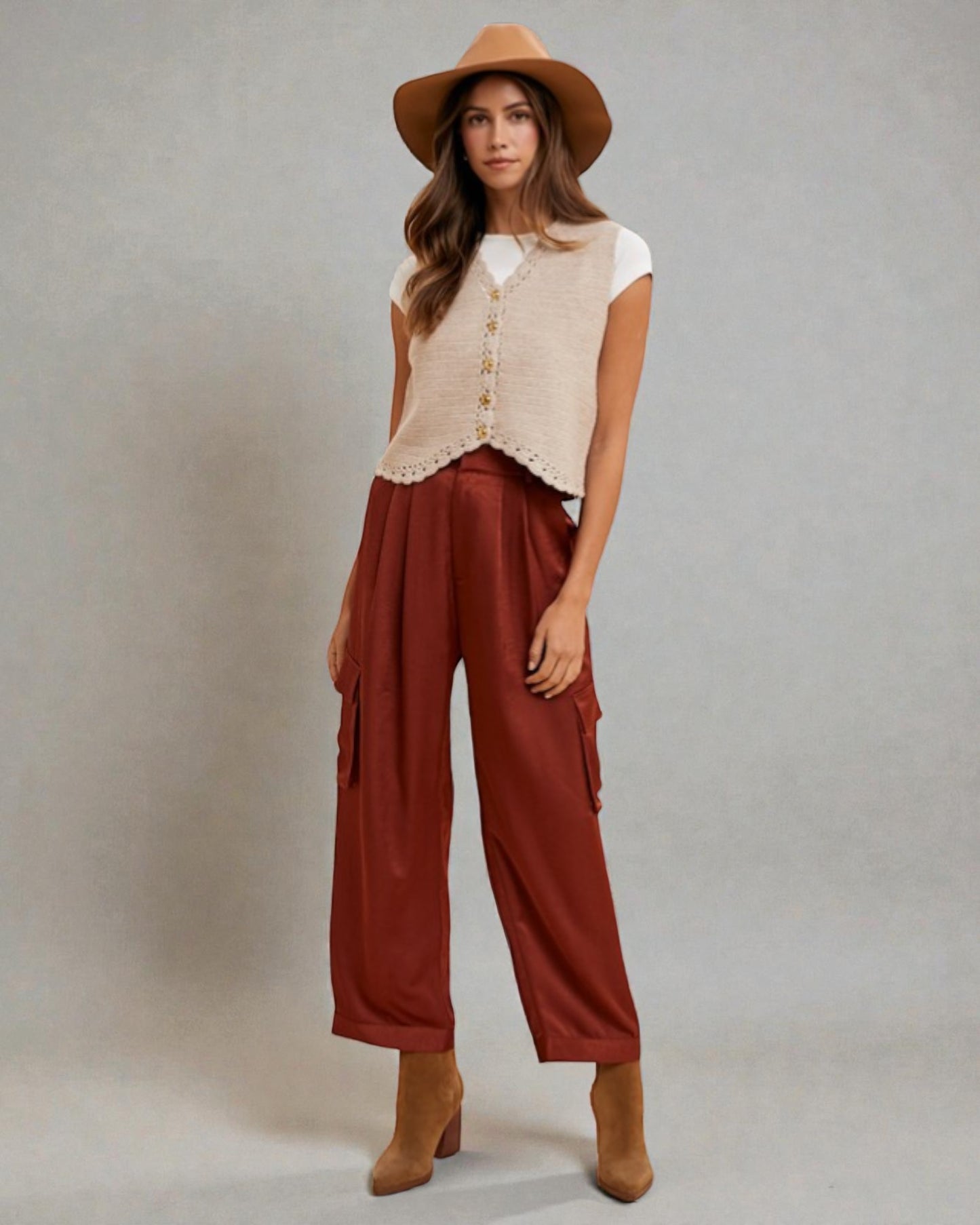 Woman wearing a beige sleeveless top, brown wide-leg pants, and a brown hat against a gray background