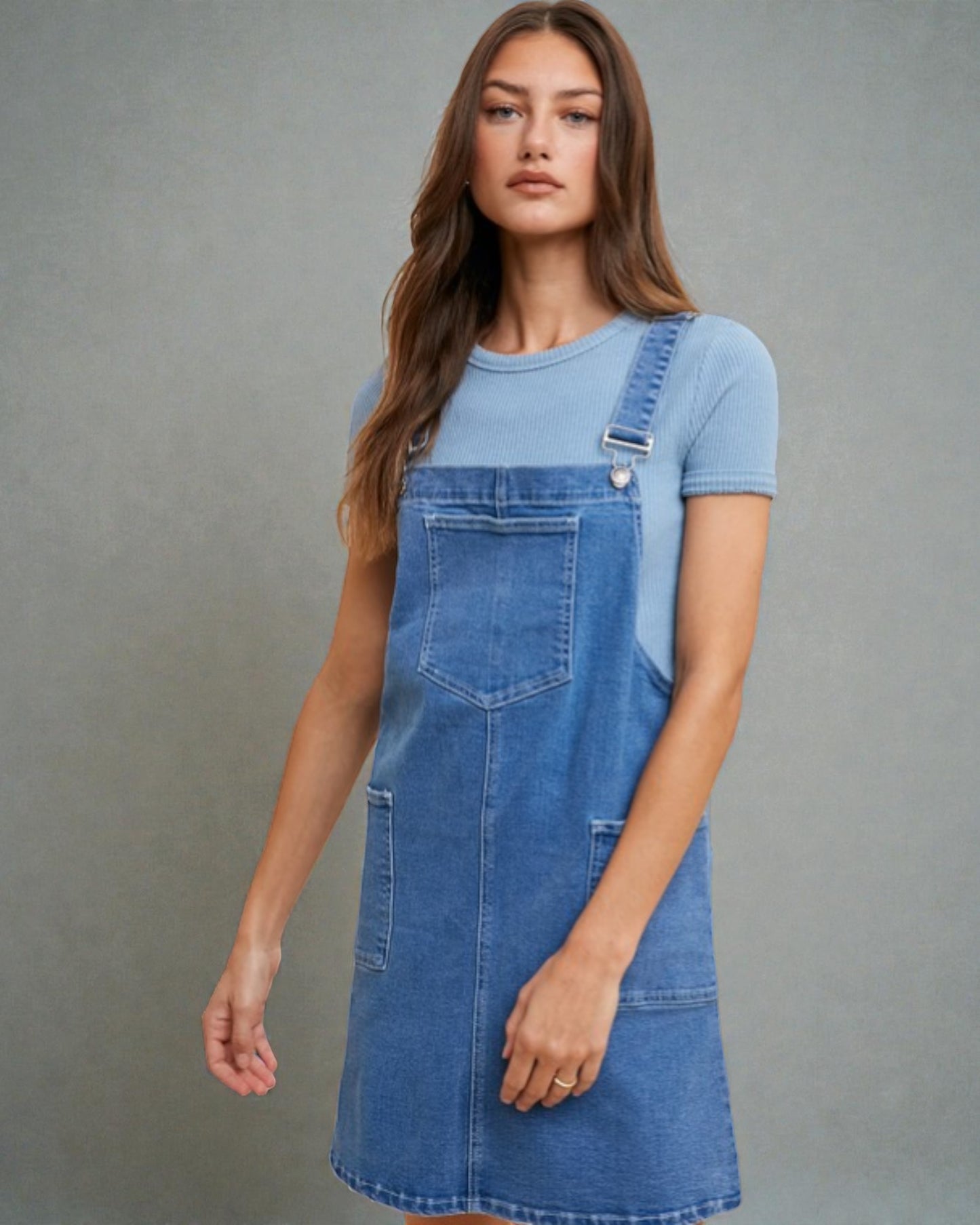 Woman wearing a blue denim dress over a light blue t-shirt against a gray background