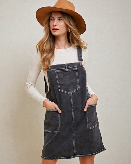 Woman wearing a denim pinafore dress and brown hat against a plain background