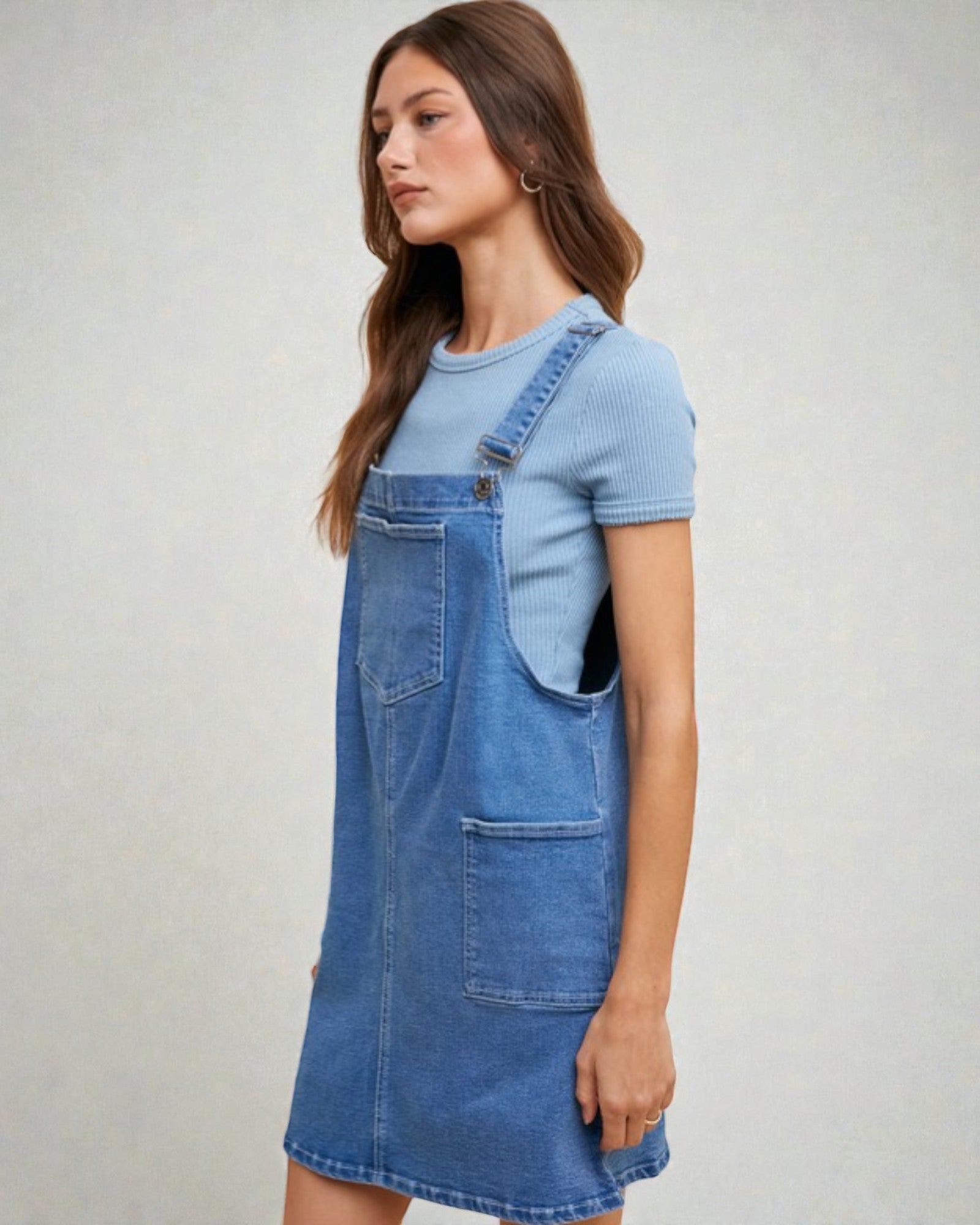 Woman wearing a blue denim dress over a light blue t-shirt on a plain background
