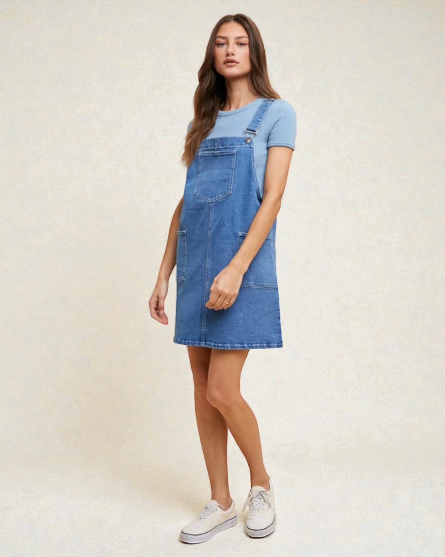 Woman wearing a blue denim dress over a light blue t-shirt on a white background