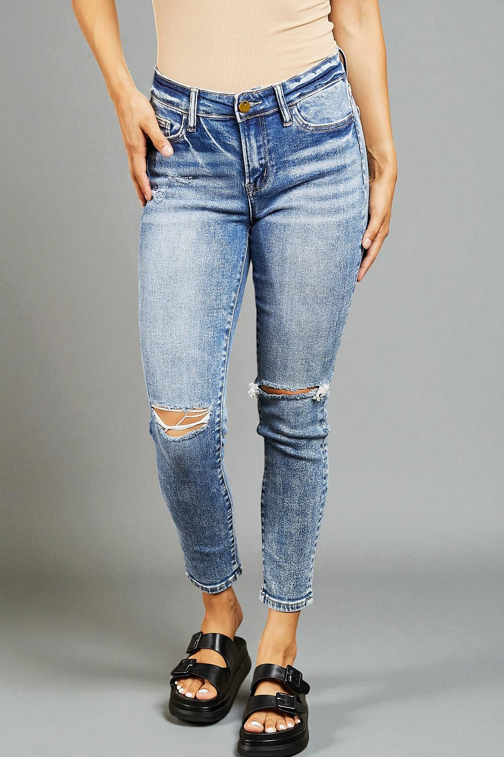 Person wearing distressed blue jeans on a gray background