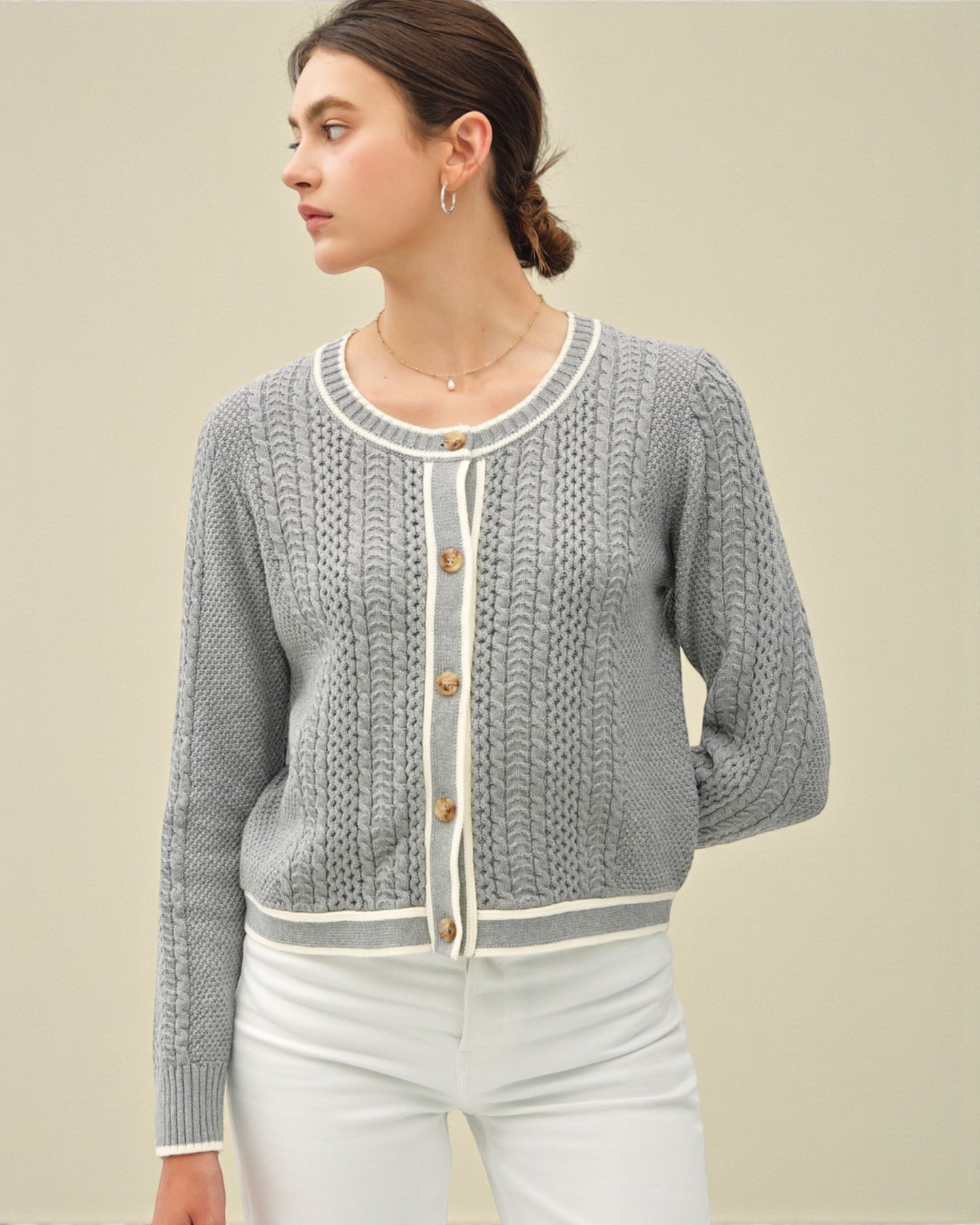 Woman wearing a gray knitted cardigan with white buttons against a beige background