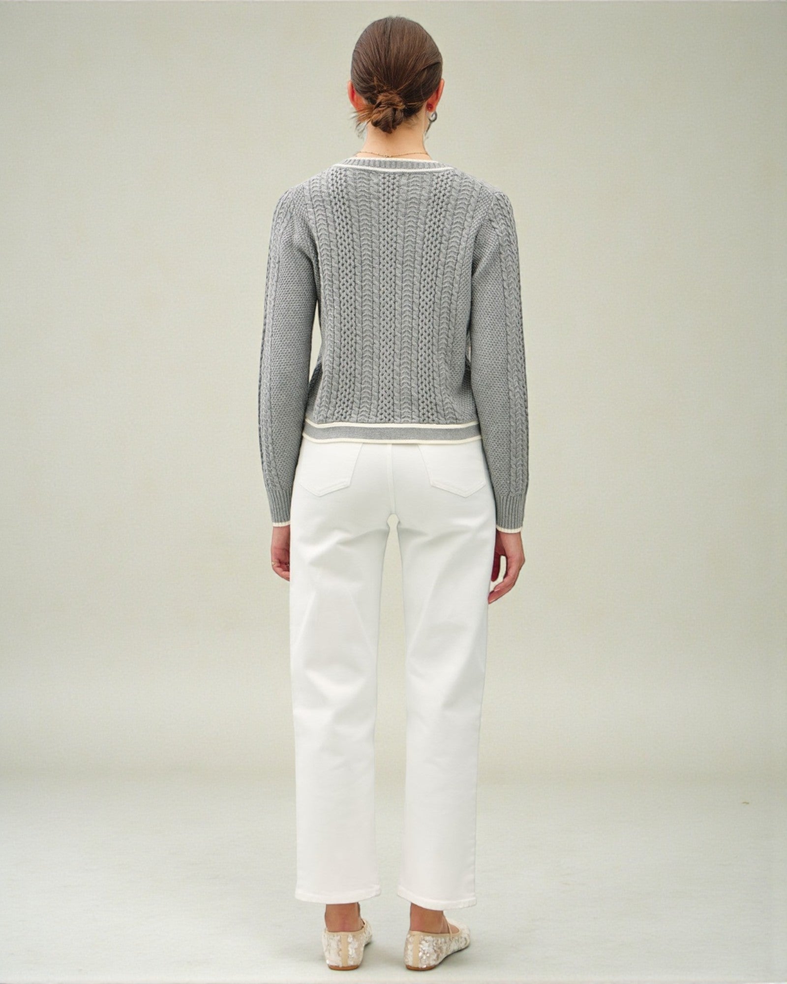 Person wearing a gray sweater and white pants on a plain background