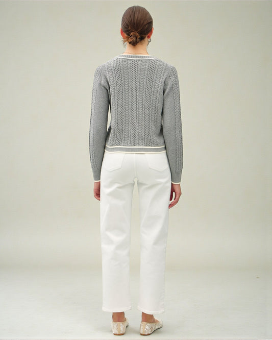 Person wearing a gray sweater and white pants on a plain background