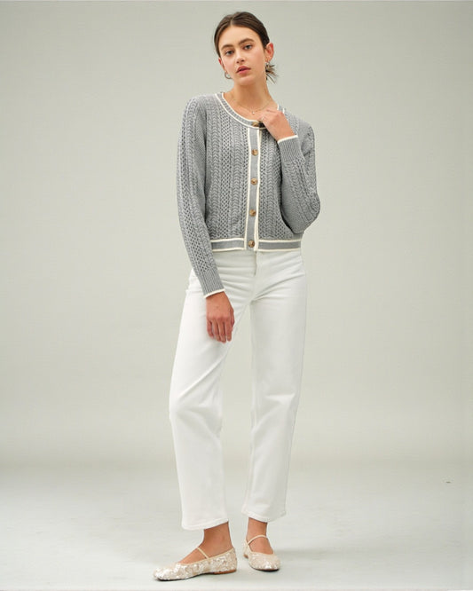 Woman wearing a gray cardigan over a white top with white pants on a plain background