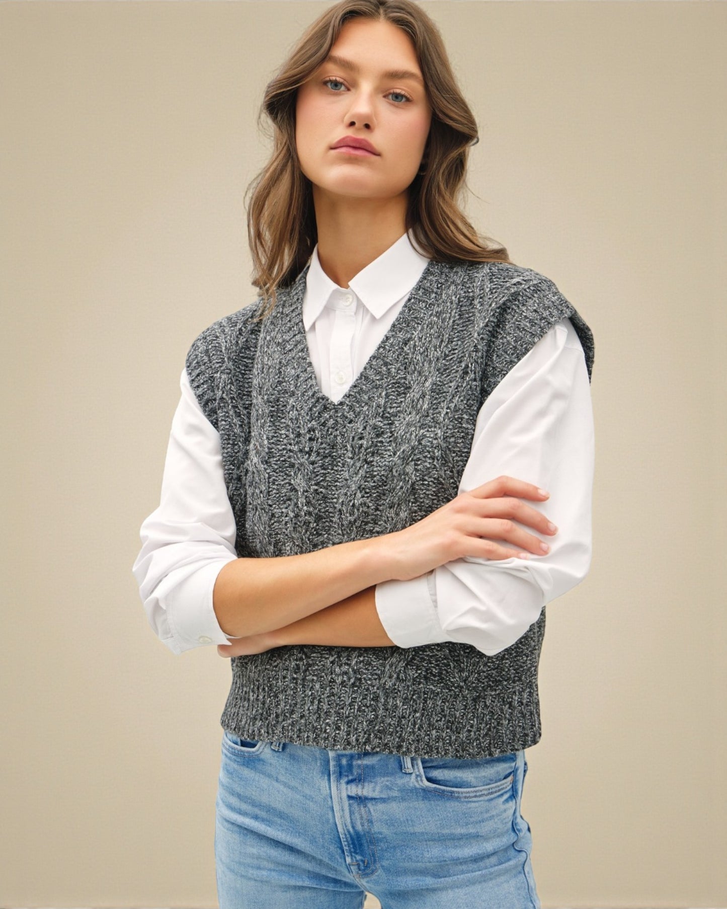 Woman wearing a gray knitted vest over a white shirt with a beige background