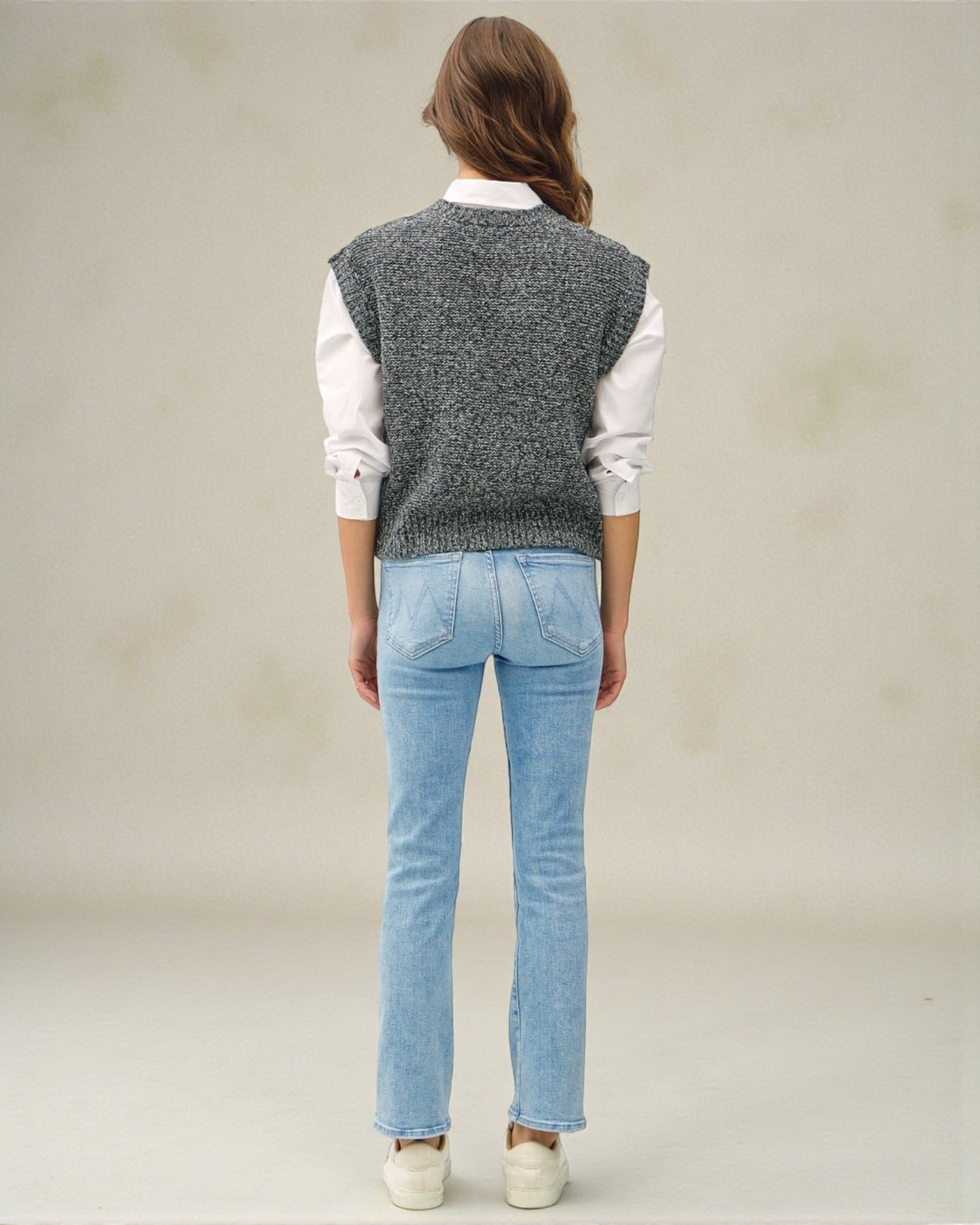 Person wearing a gray knitted vest, white shirt, and blue jeans on a plain background