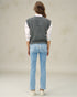 Person wearing a gray knitted vest, white shirt, and blue jeans on a plain background