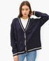A woman modeling a dark purple cable-knit cardigan sweater with cream-colored trim and buttons, worn over a white t-shirt and blue jeans against a plain white background.