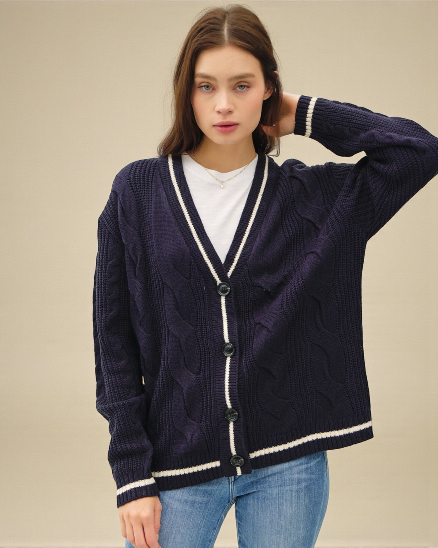 Woman wearing a navy blue cardigan with white trim on a beige background