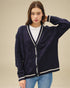Woman wearing a navy blue cardigan with white trim on a beige background