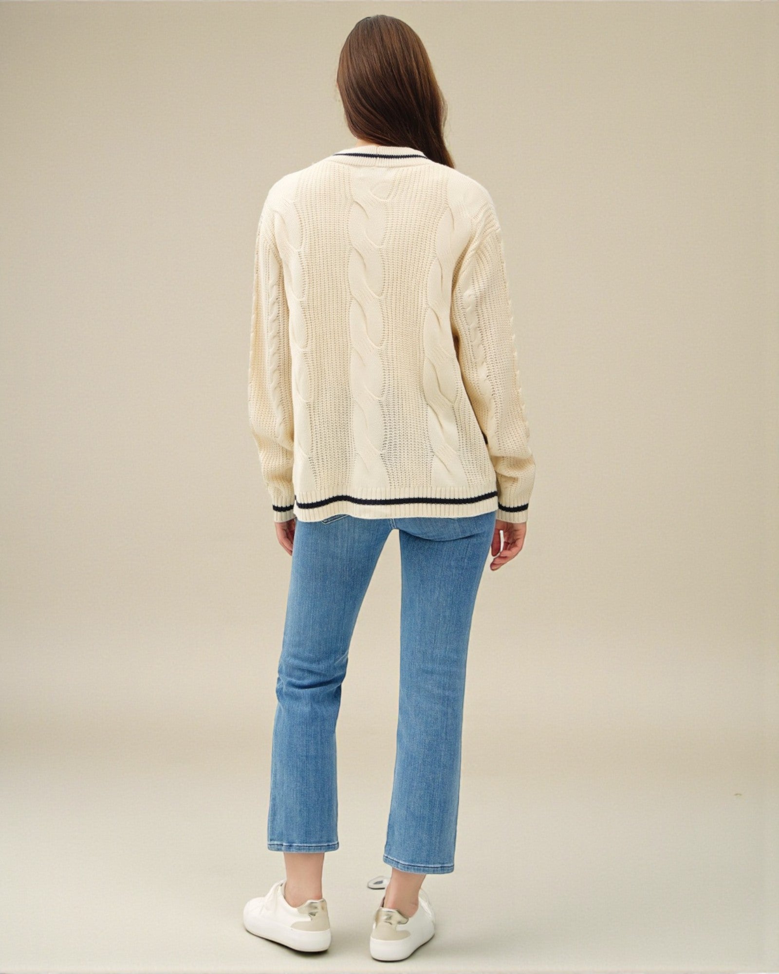 Person wearing a cream sweater and blue jeans on a plain background