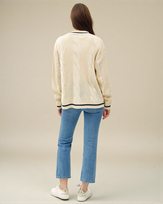 Person wearing a cream sweater and blue jeans on a plain background
