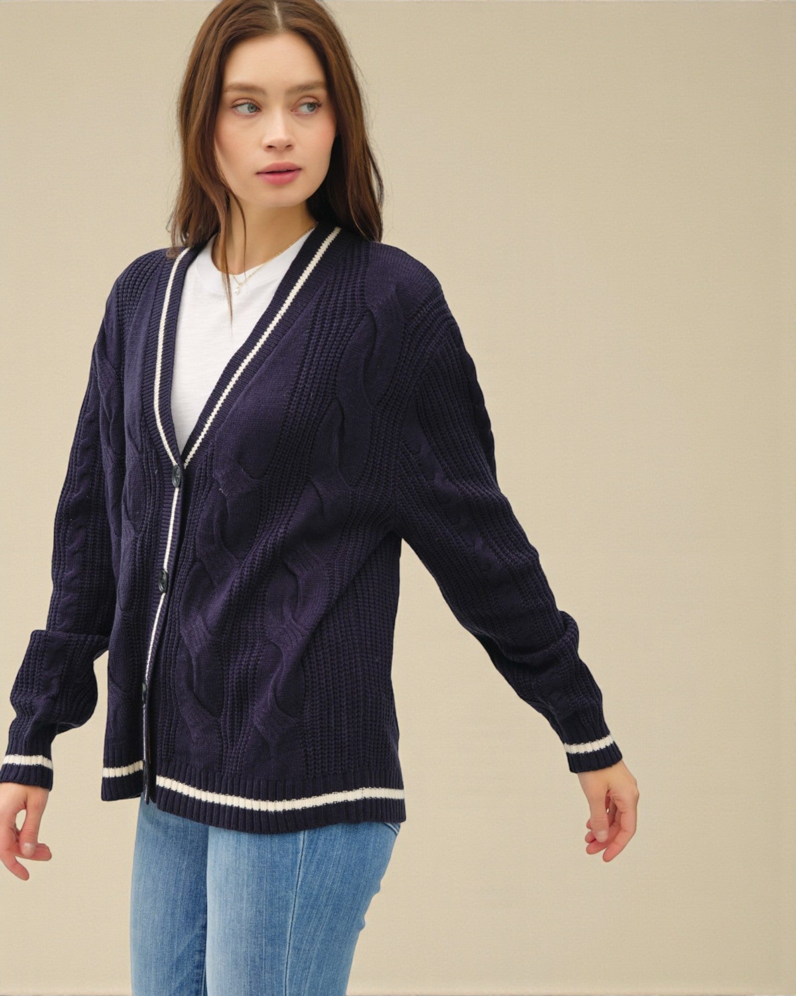Woman wearing a navy cardigan with white trim on a beige background