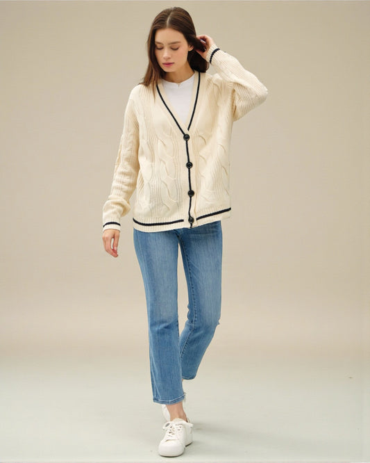 Woman wearing a cream cardigan with black buttons, white sneakers, and blue jeans on a beige background