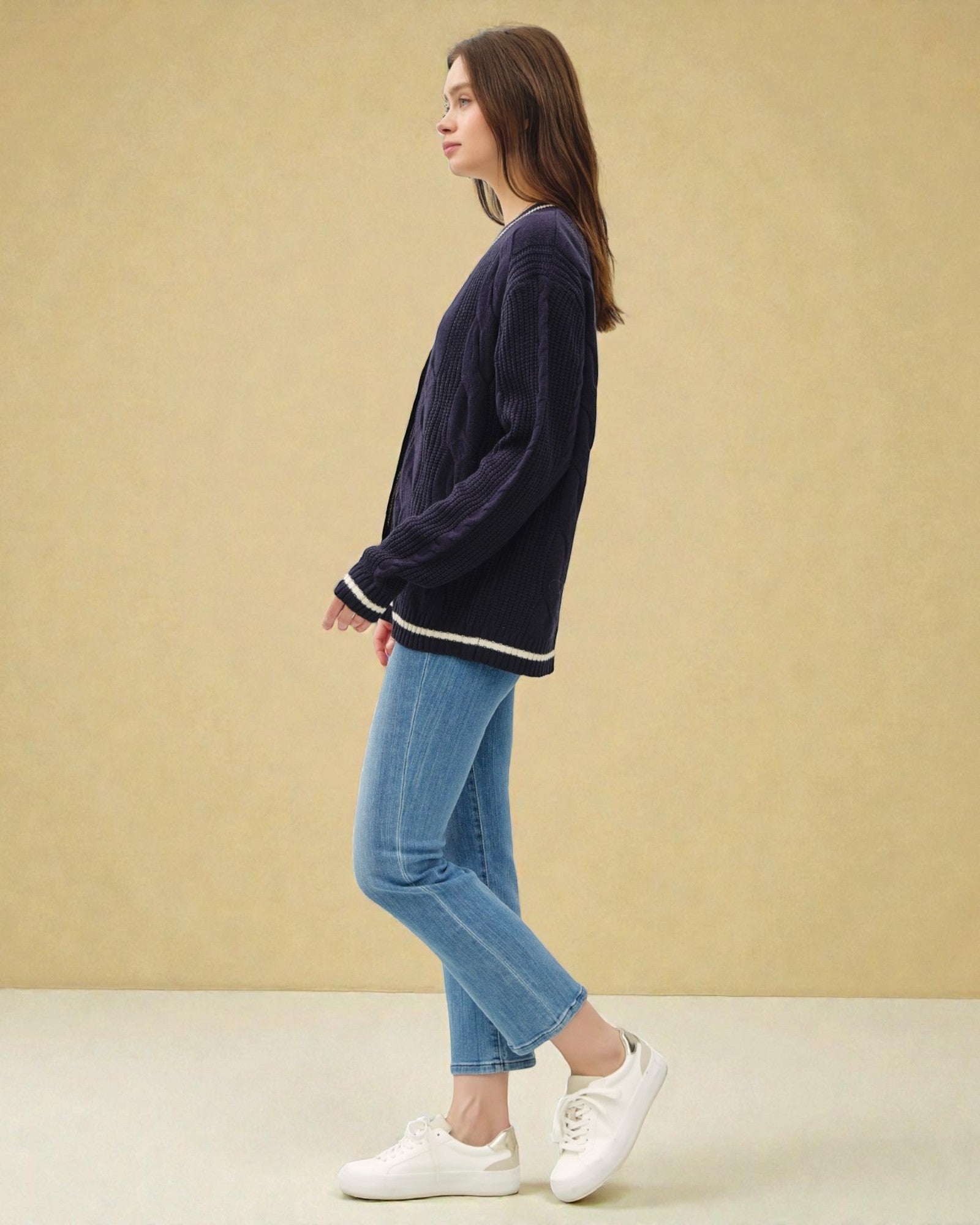 Woman wearing a navy sweater, blue jeans, and white sneakers against a beige background