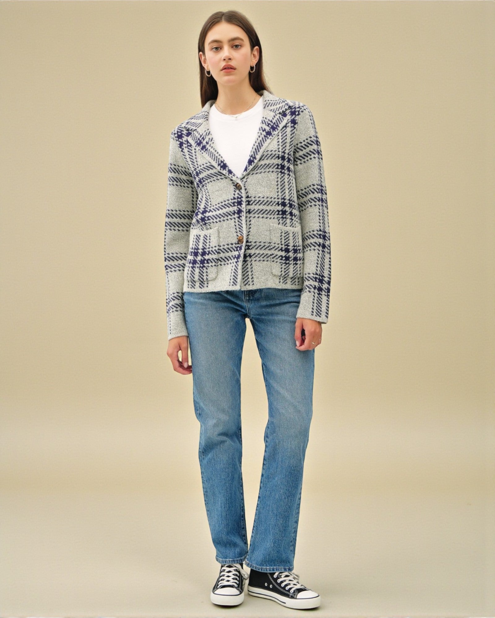 Person wearing a plaid jacket and blue jeans on a beige background