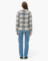 A woman viewed from the back wearing a cream-colored plaid blazer with navy and gray lines, paired with blue jeans and black sneakers, against a plain white studio background.