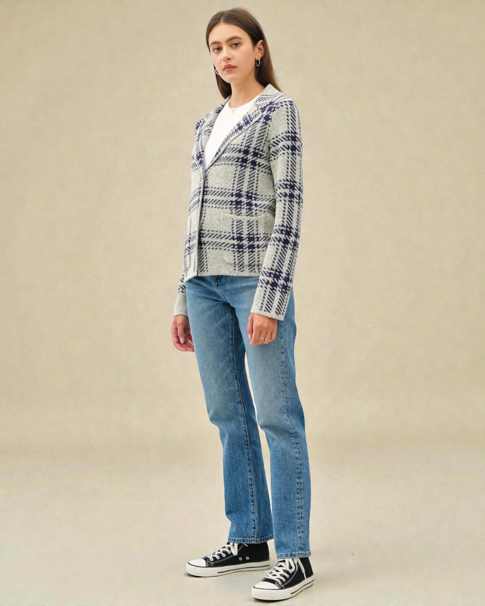 Person wearing a plaid jacket, white shirt, blue jeans, and black sneakers on a beige background