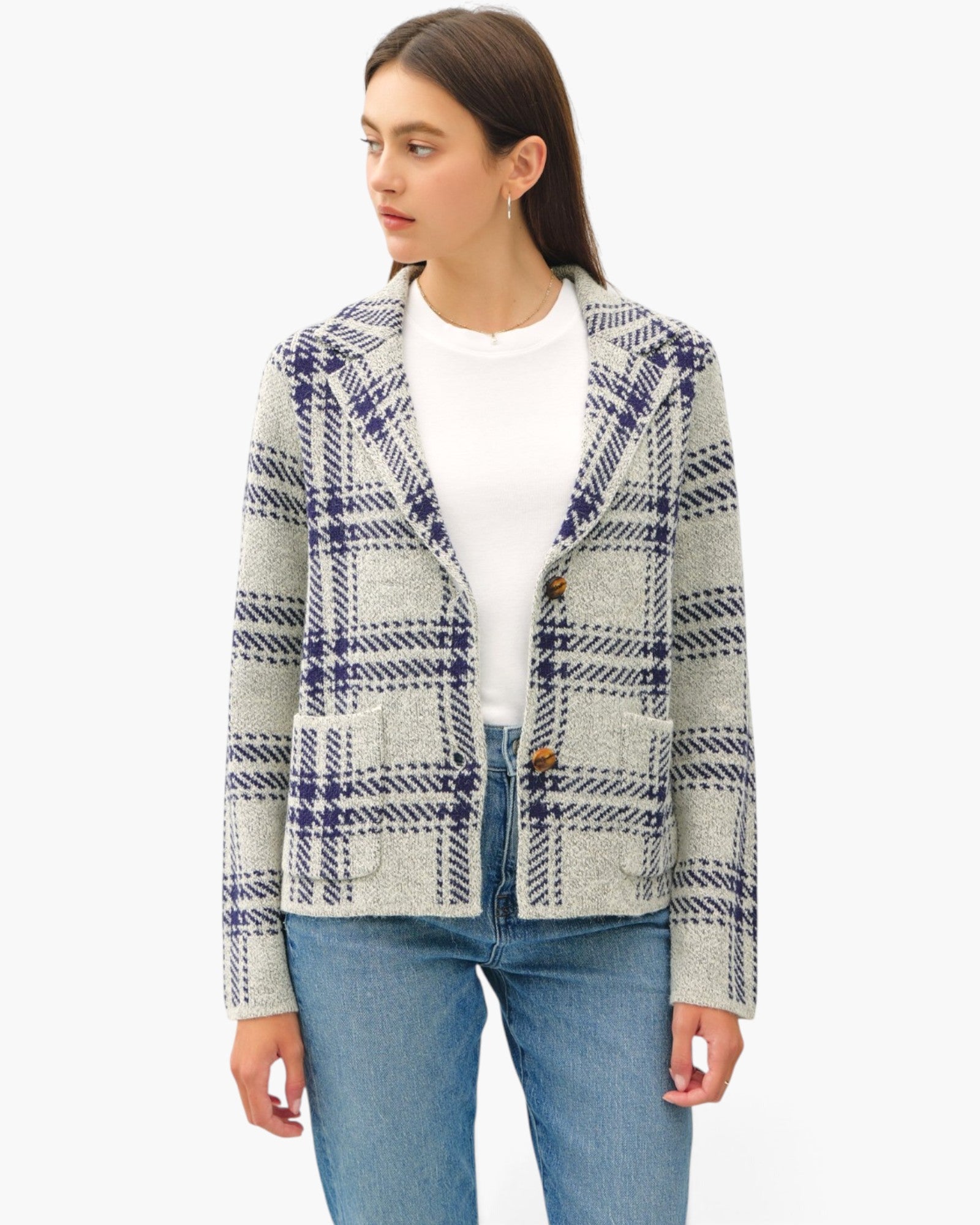 A woman modeling a textured tweed blazer with a navy and gray plaid pattern, worn over a white mock neck top and blue jeans, against a plain white background.