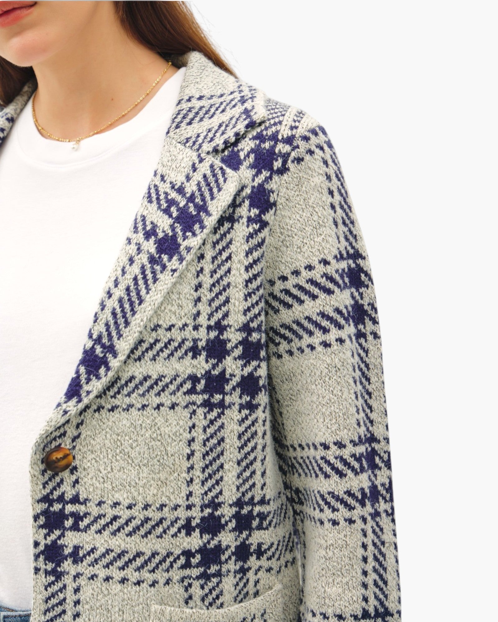 A close-up of a woman wearing a textured tweed blazer with a gray, white, and navy blue plaid pattern over a white top.