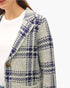 A close-up of a woman wearing a textured tweed blazer with a gray, white, and navy blue plaid pattern over a white top.