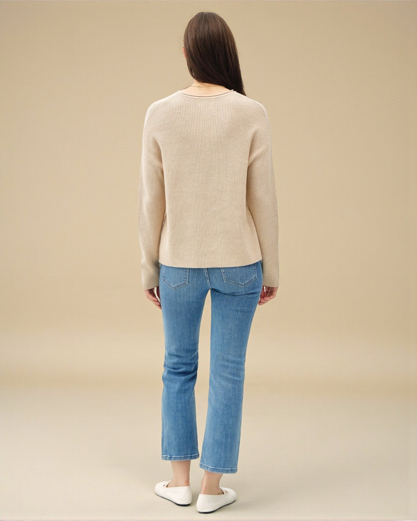 Person wearing a beige sweater and blue jeans on a beige background