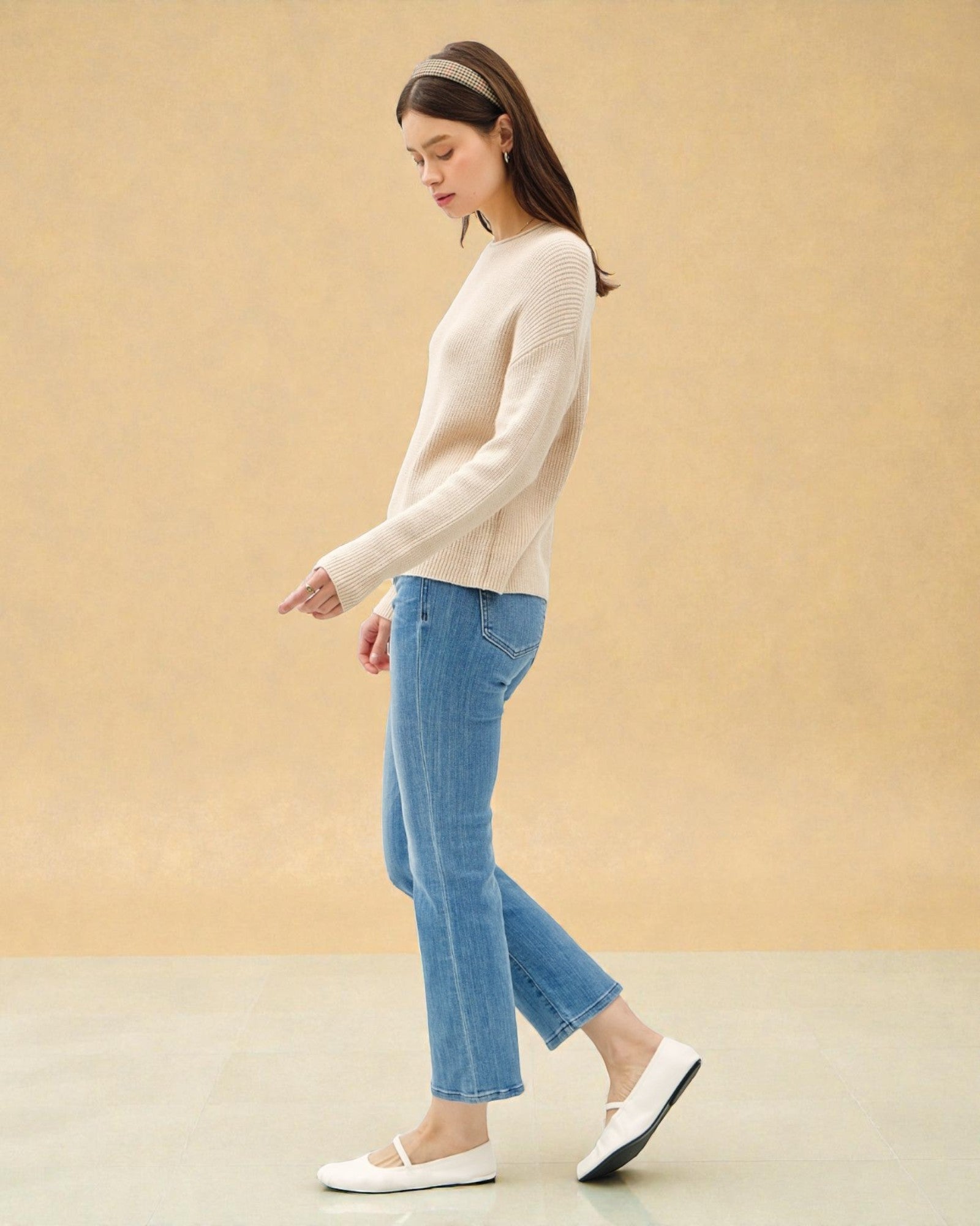 Woman wearing a beige sweater and blue jeans against a beige background