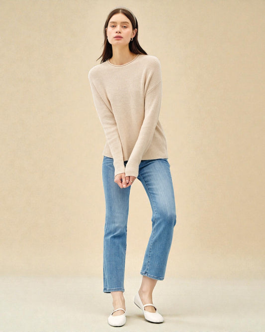 Woman wearing a beige sweater and blue jeans on a beige background