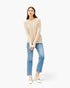 A woman modeling a light beige knit sweater and light blue cropped jeans with white Mary Jane shoes, photographed against a clean white studio background.