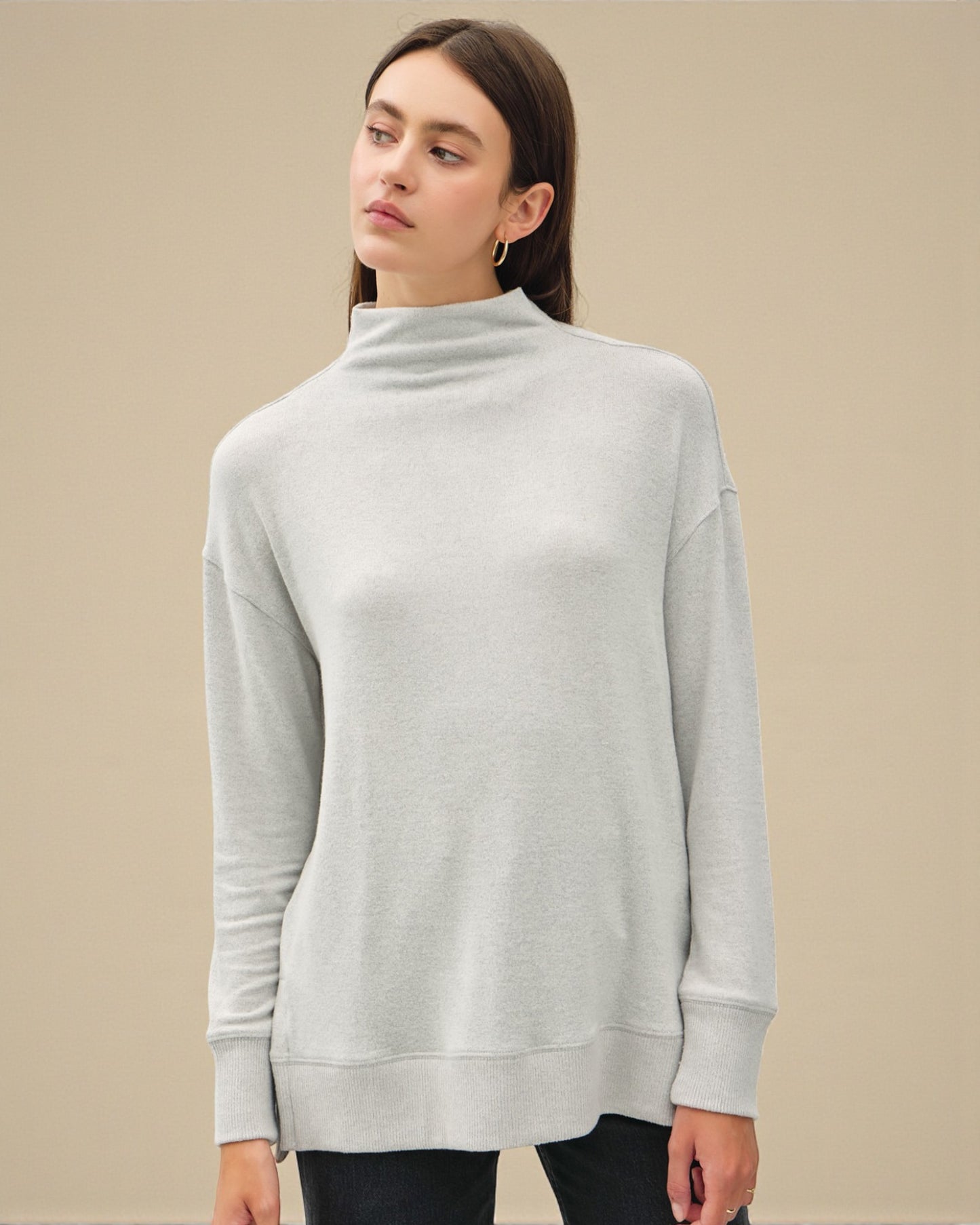 Woman wearing a light gray turtleneck sweater against a beige background
