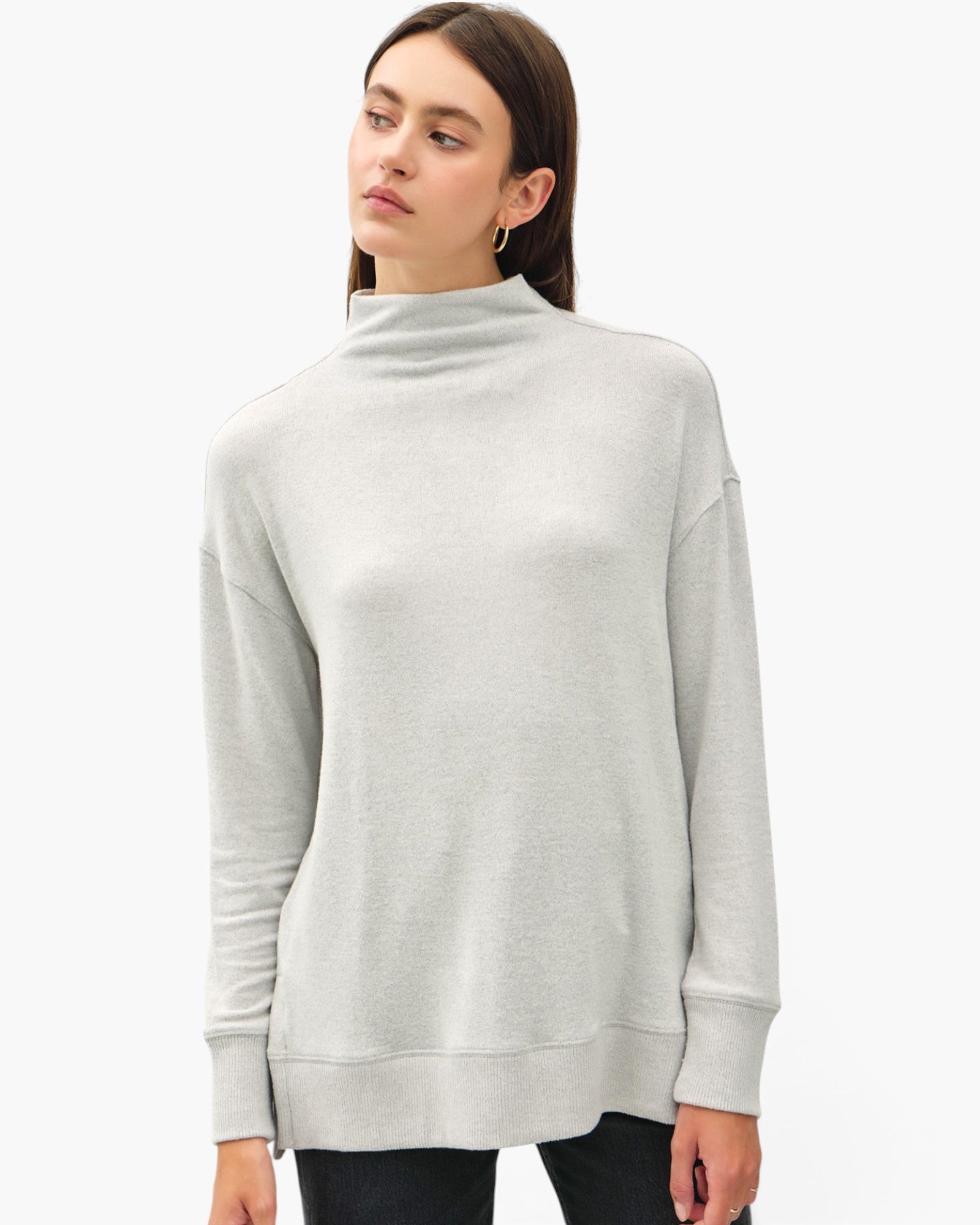 A woman wearing a light gray heathered mock neck sweater, shown from the waist up against a plain white studio background.
