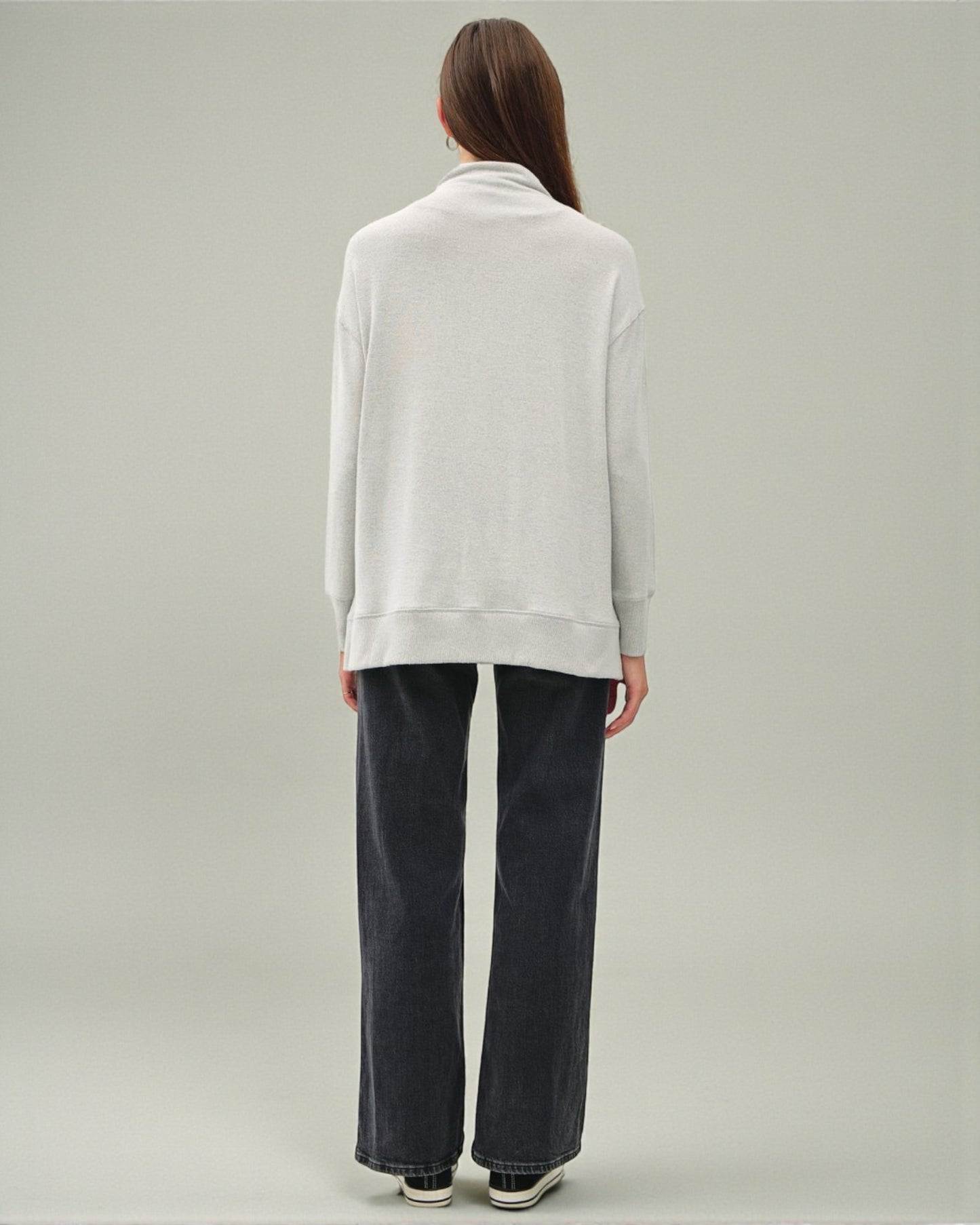 Person wearing a white sweater and dark pants on a plain background