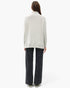A model shown from the back wearing a light gray heathered cowl-neck sweatshirt and dark charcoal wide-leg jeans against a plain white studio background.