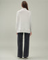 Person wearing a white sweater and dark pants on a plain background