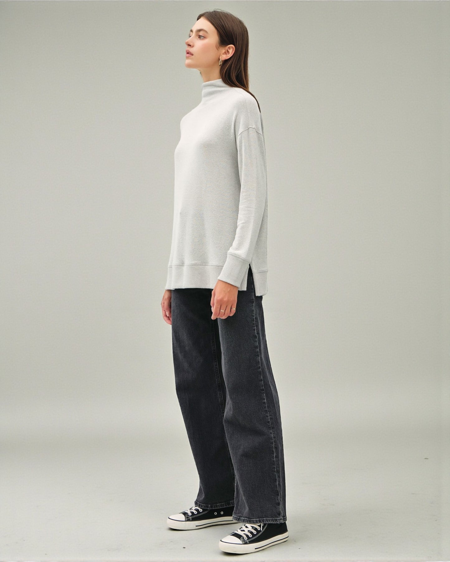 Person wearing a light gray sweater and dark jeans on a plain background