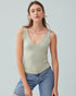 Woman wearing a green tank top and blue jeans against a light gray background