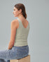 Woman wearing a light green tank top and blue jeans sitting on a box against a gray background