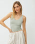 Woman wearing a light green tank top and white pants against a plain background