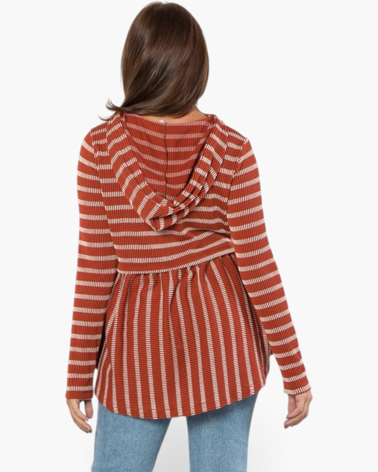 A woman viewed from the back wearing a rust-orange and white striped long-sleeve top with a draped cowl neckline and a peplum waist, paired with light blue jeans against a plain white background.