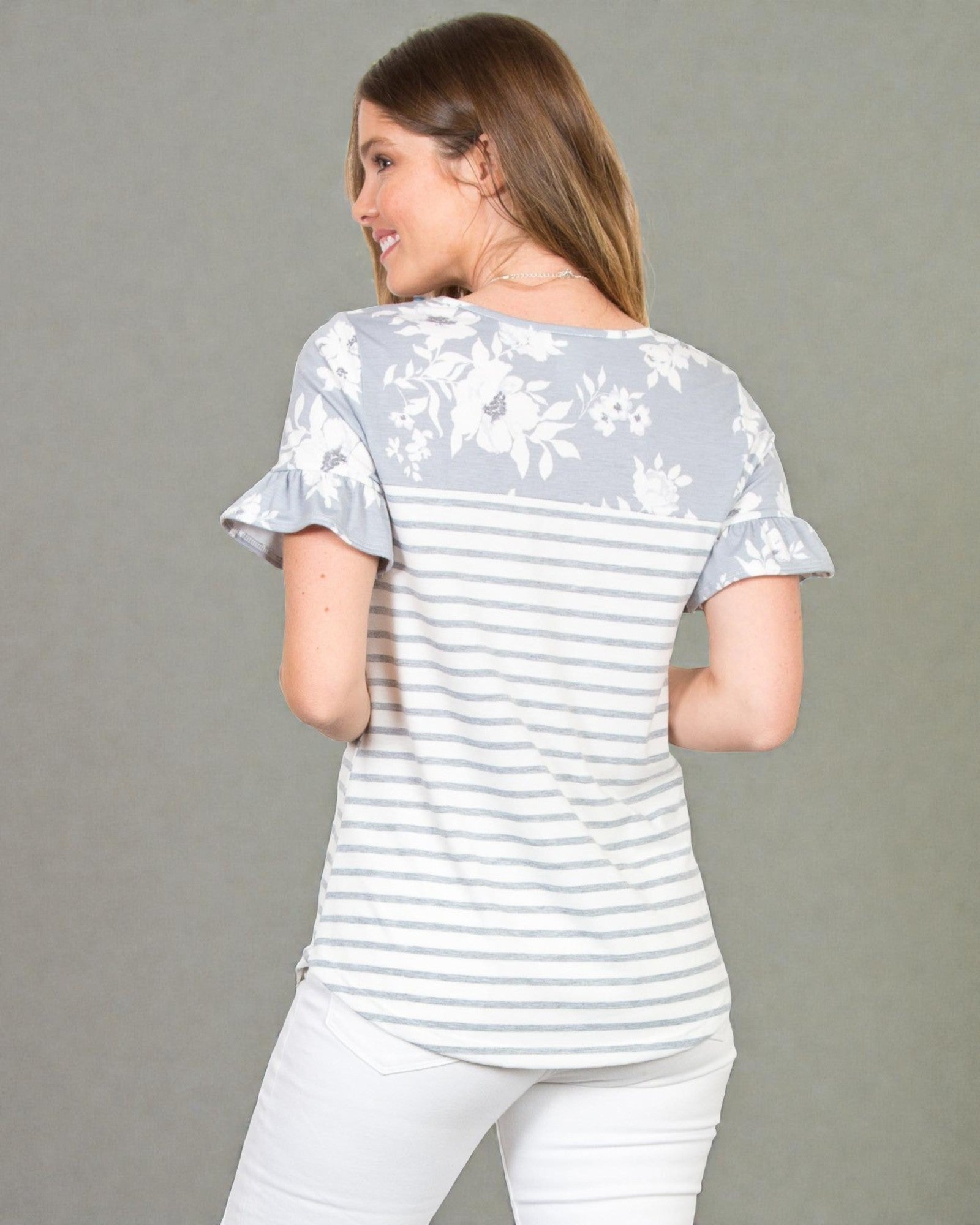 Woman wearing a light gray and white striped shirt with floral sleeves on a gray background