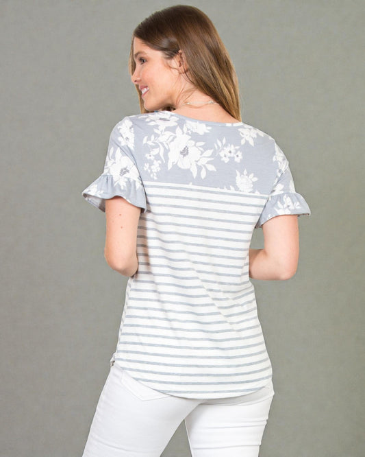 Woman wearing a light gray and white striped shirt with floral sleeves on a gray background