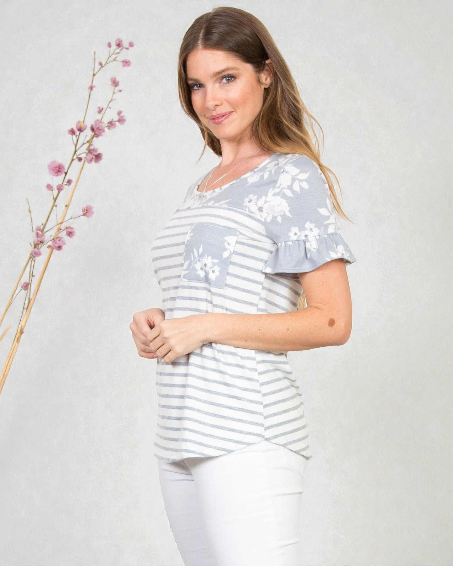 Woman wearing a gray and white striped shirt with floral patterns on a plain background