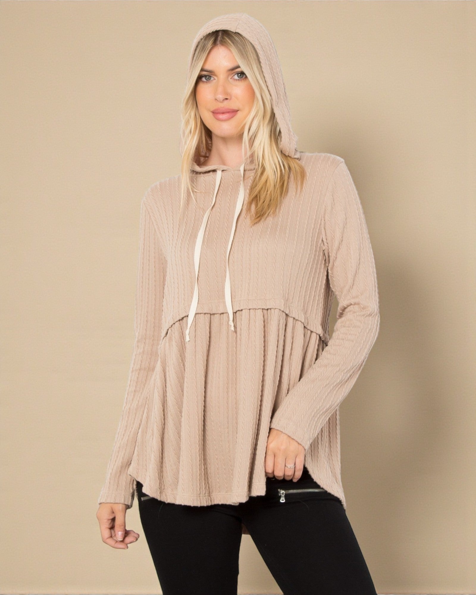 Woman wearing a beige hooded top against a beige background