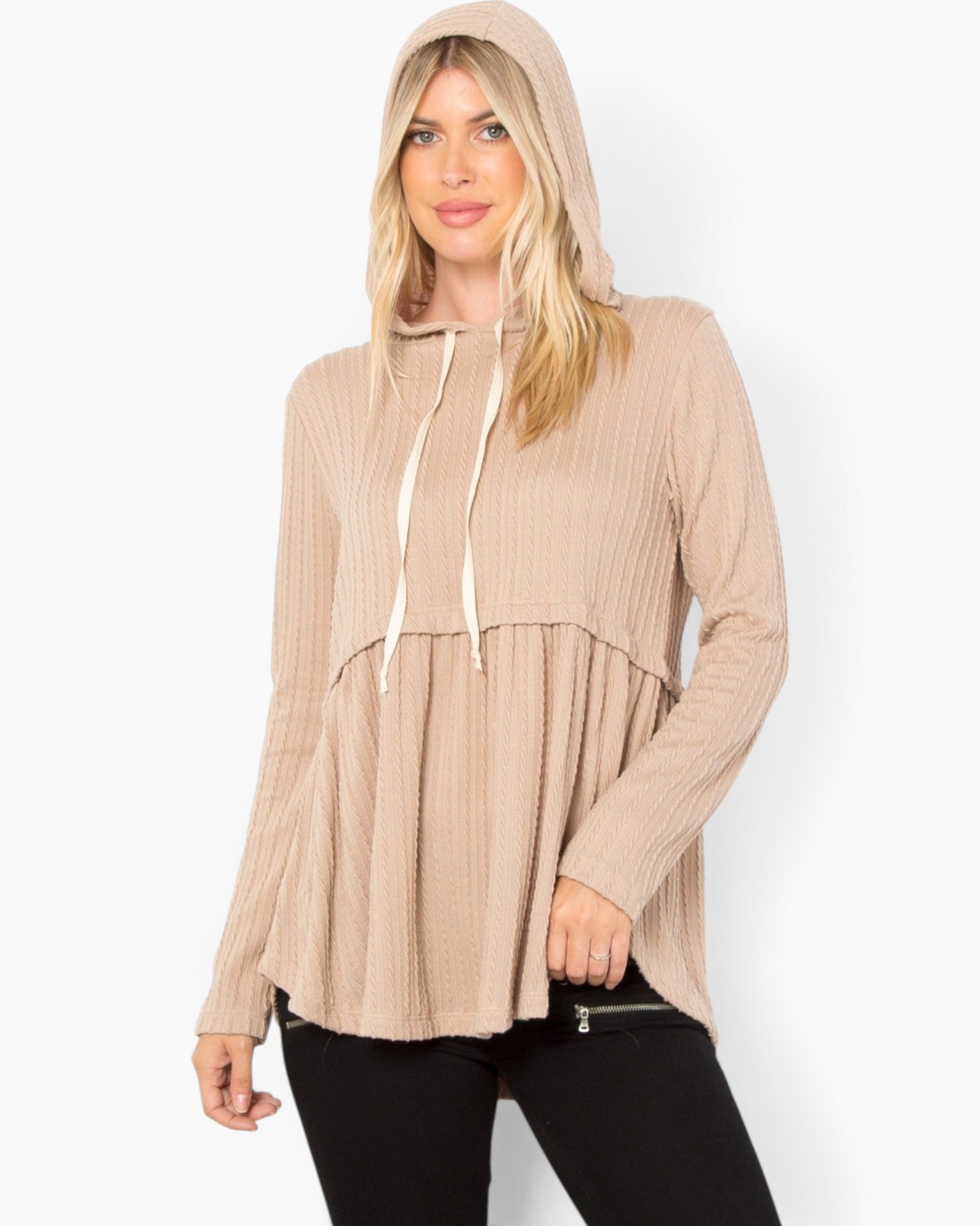 A woman wearing a beige ribbed knit hooded long-sleeve top with cream drawstrings and black pants, photographed against a plain light gray studio background.