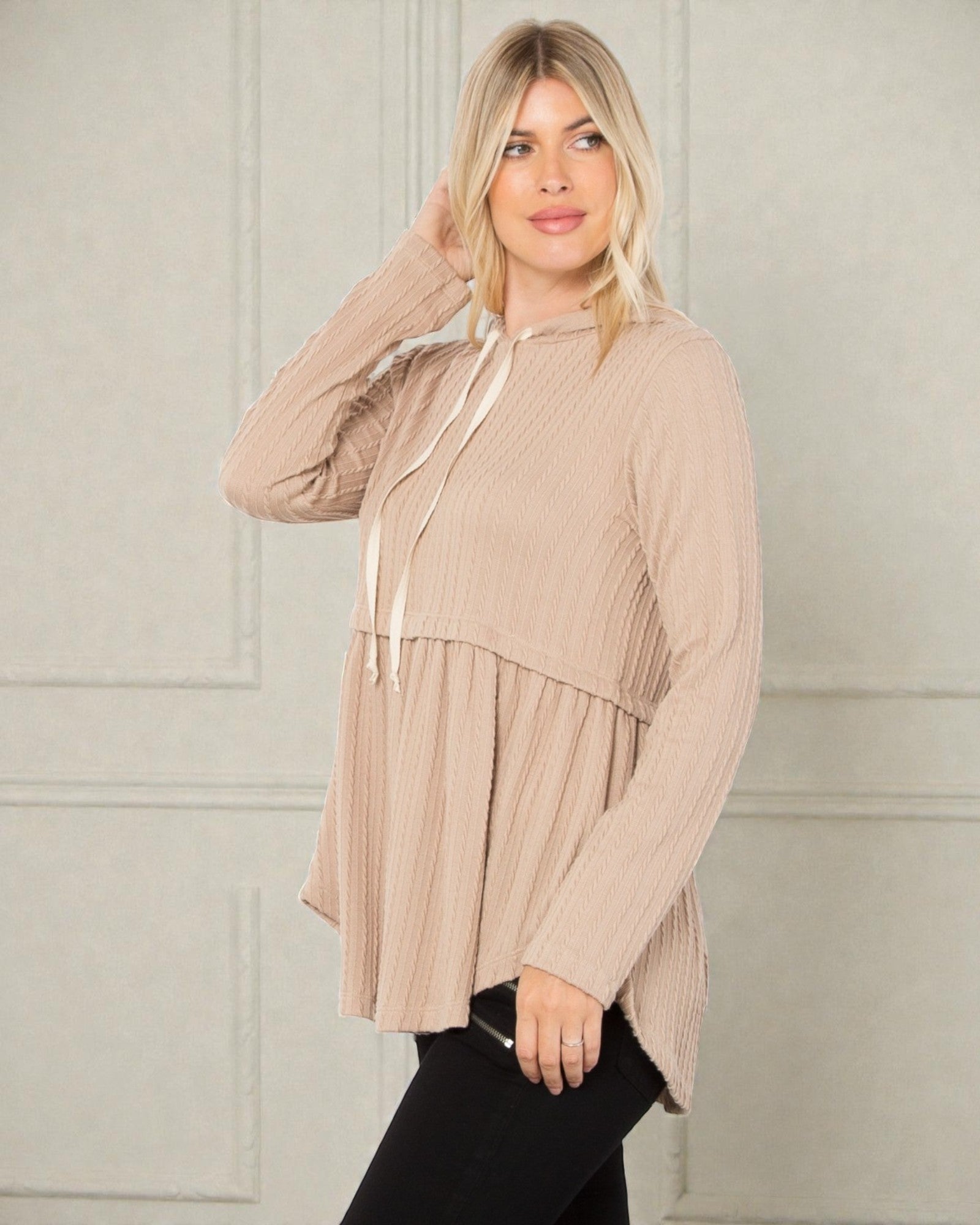 Woman wearing a beige long-sleeve top with a subtle pattern against a neutral background