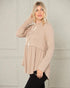 Woman wearing a beige long-sleeve top with a subtle pattern against a neutral background