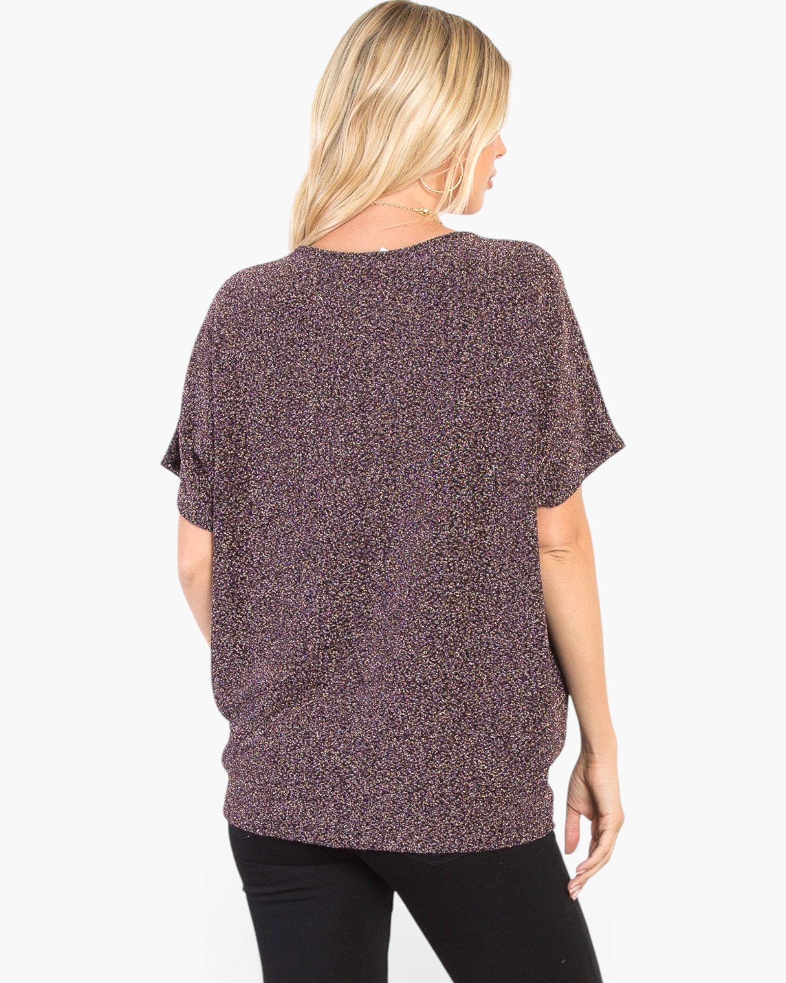 A woman shown from the back wearing a loose, short-sleeve knit top with a mottled purple and black pattern, paired with black pants, against a plain white background.